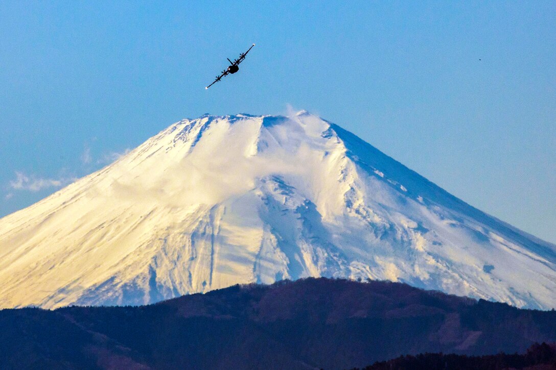 An aircraft flies above a giant snow-covered mountain.
