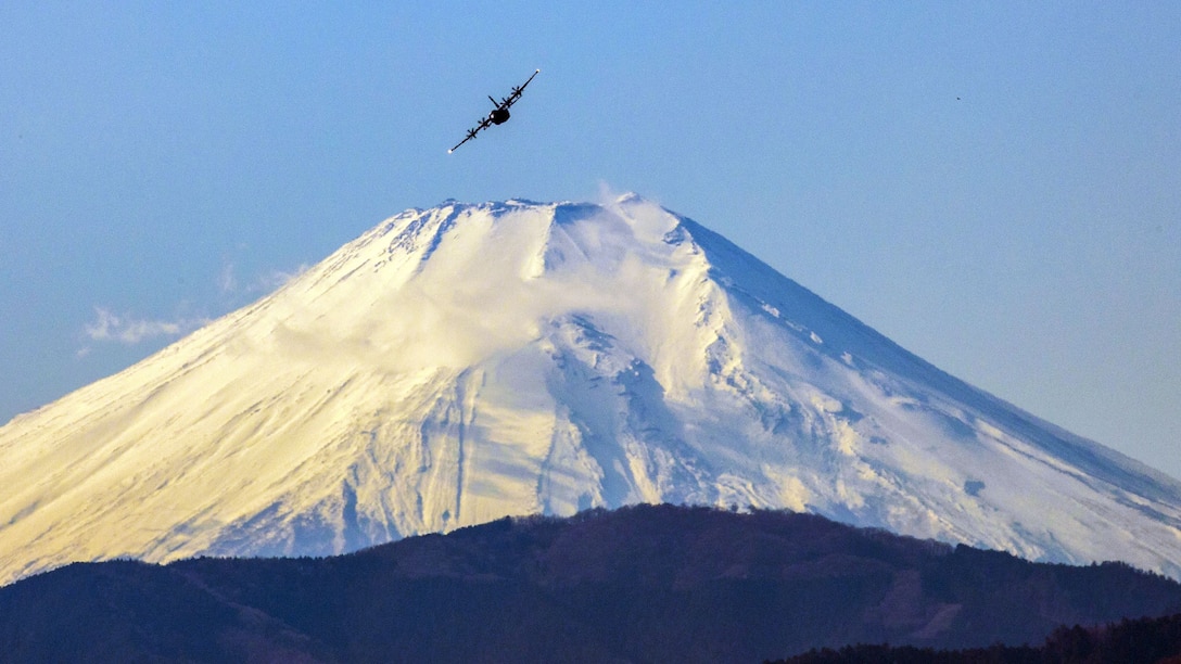 An aircraft flies above a giant snow-covered mountain.