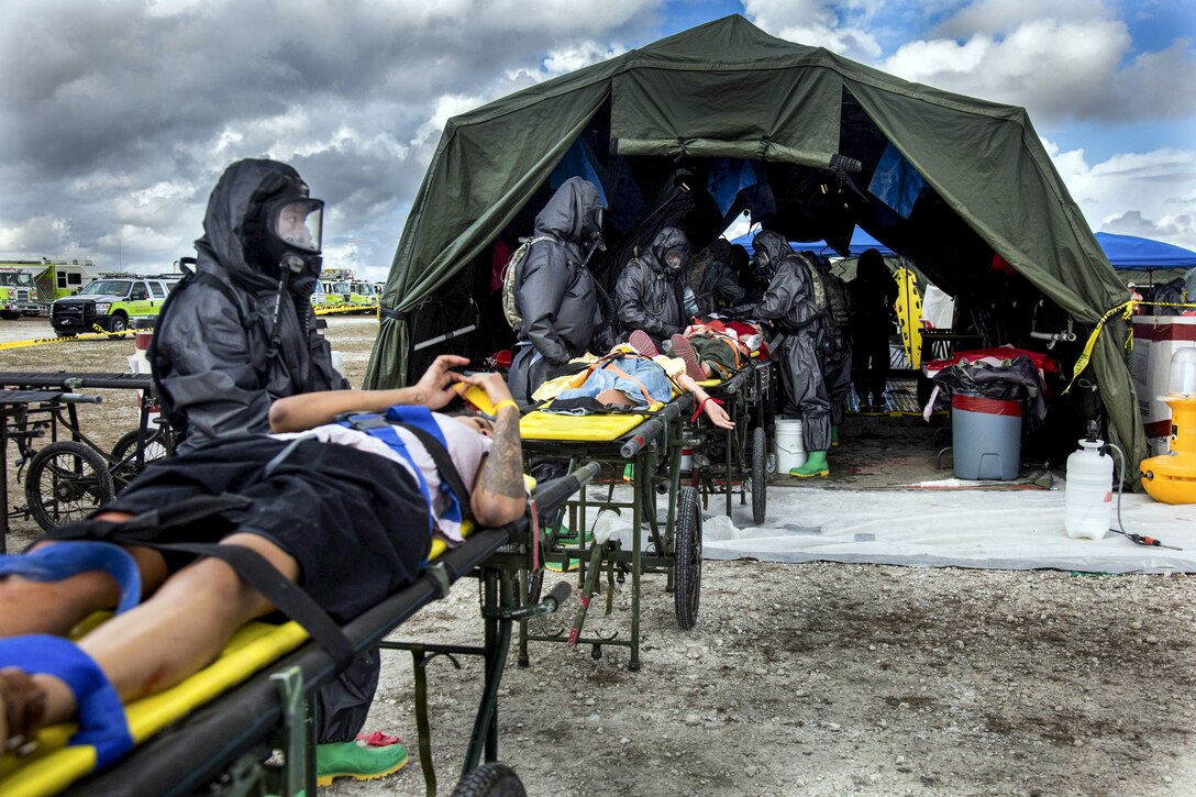 Soldiers wearing full-body black protective suits and masks tend to mock patients on stretchers by a tent.