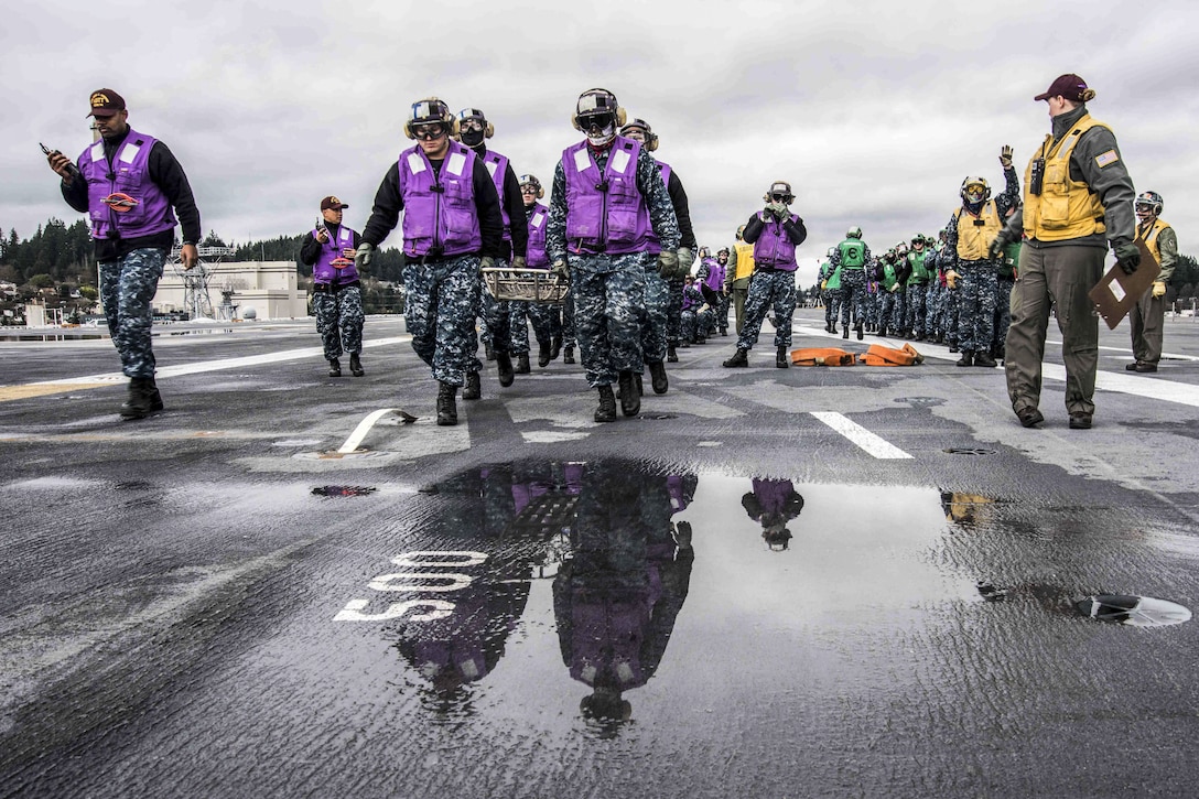 Sailors carry a stretcher on a flight deck.