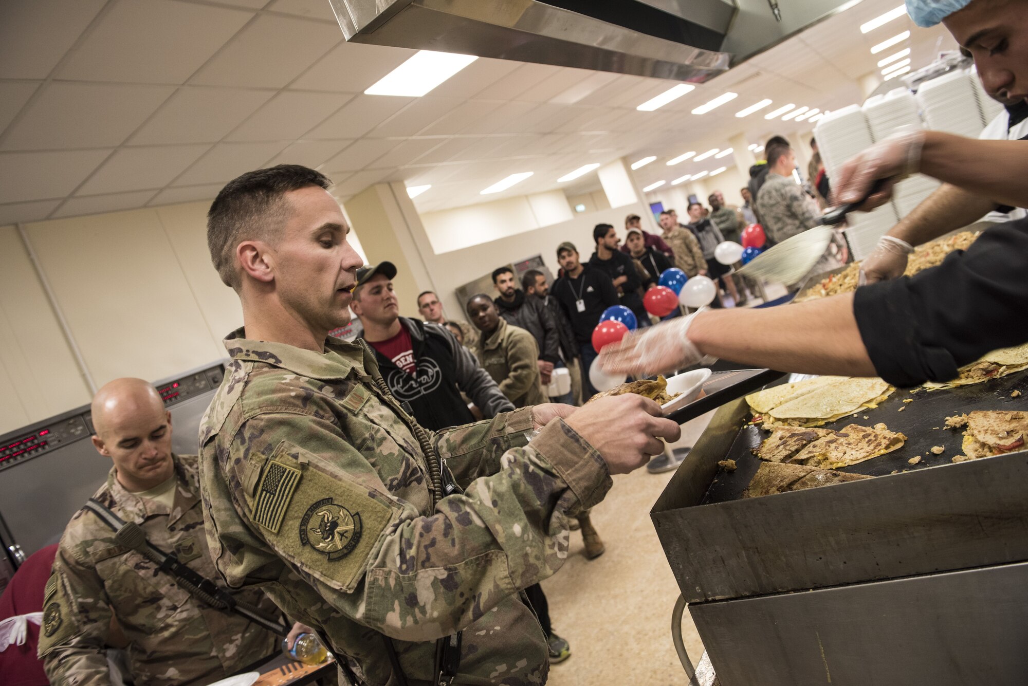 Airmen from the 332d Air Expeditionary Wing line up for a meal during the grand re-opening of the “Red Tail” dining facility January 11, 2018 in Southwest Asia. During renovations, the facility added a new grill, which will increase the variety of menu items offered to deployed service members. (U.S. Air Force photo by Staff Sgt. Joshua Kleinholz)