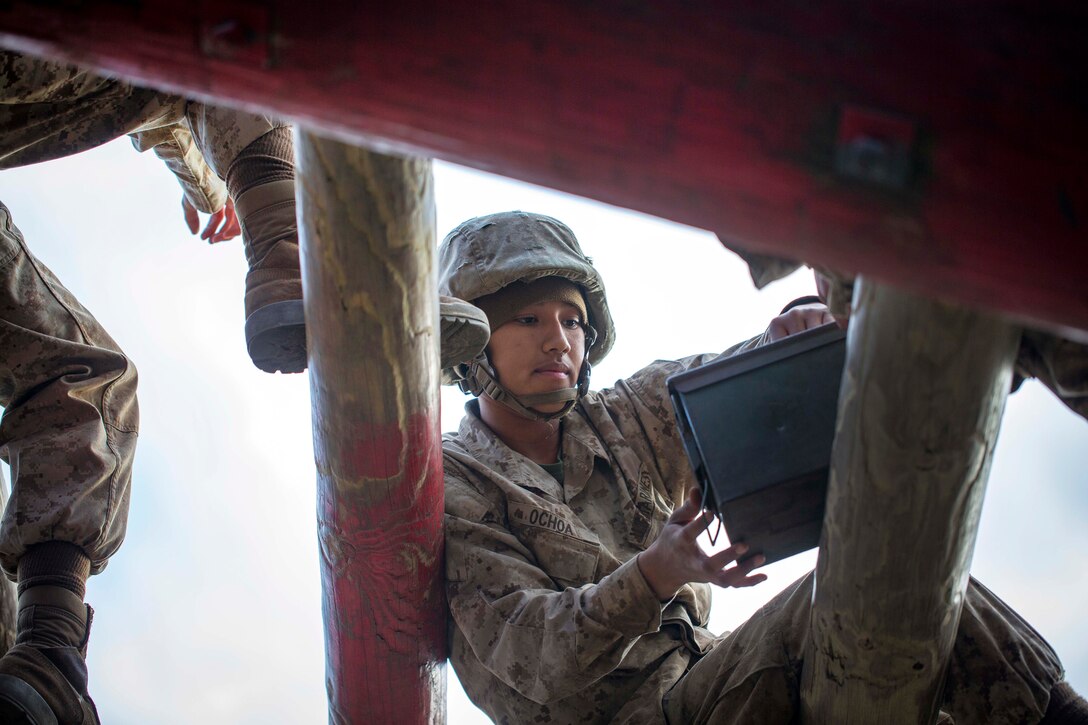 A Marine holds an ammo can while sitting on a log.