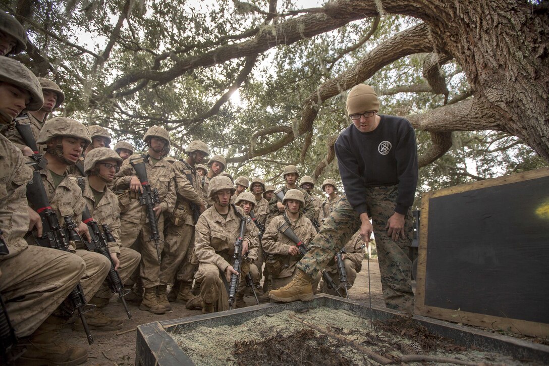 A Marine talks to other Marines kneeling in a semi-circle.