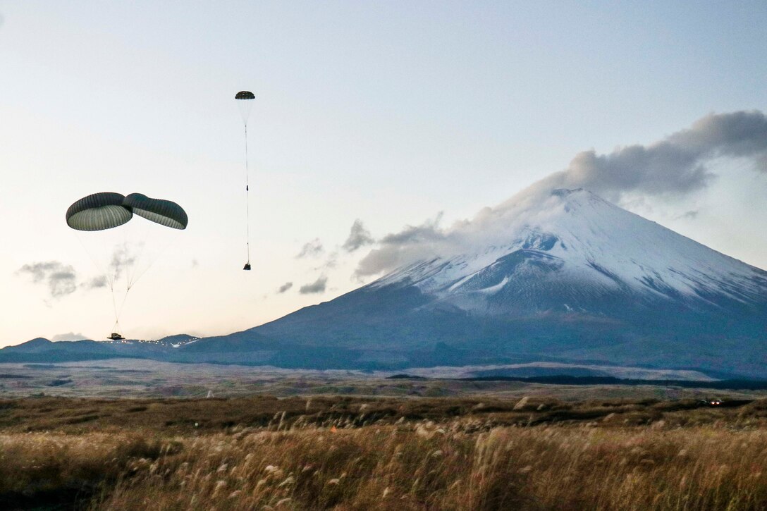 Packages drift to the ground on parachutes with a mountain in the background.