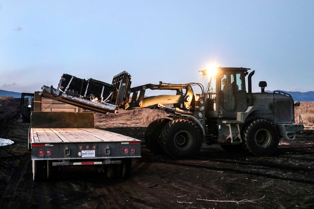 A Marine operates a heavy forklift to place heavy bundles onto the back of a truck.