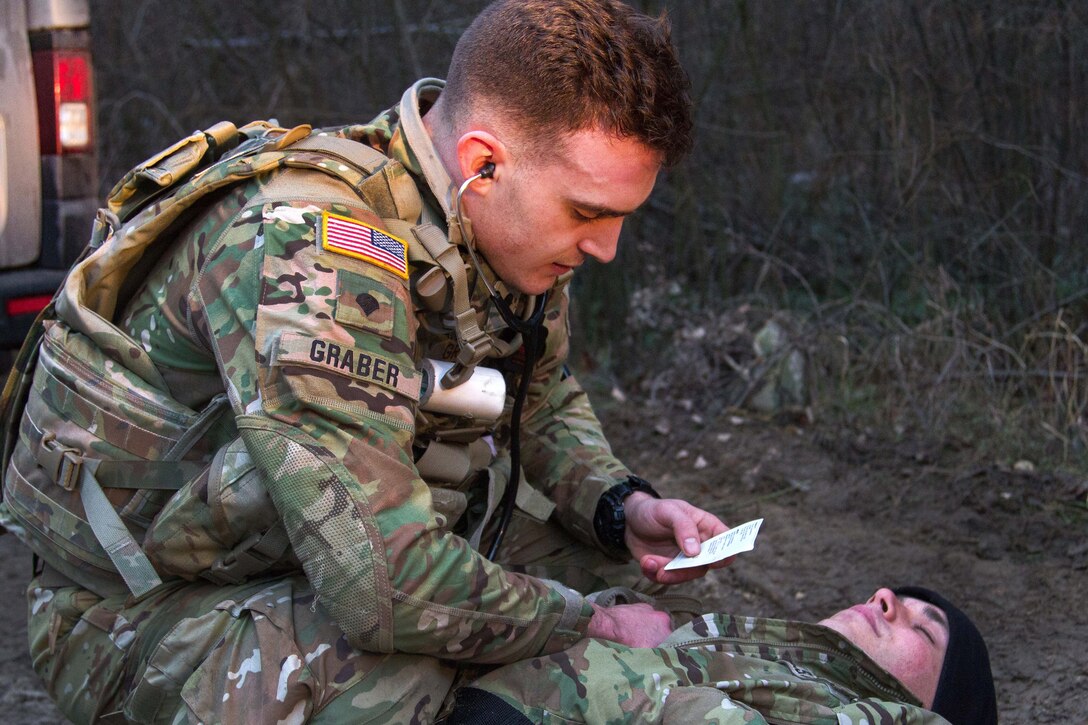 A soldier kneels next to a person.