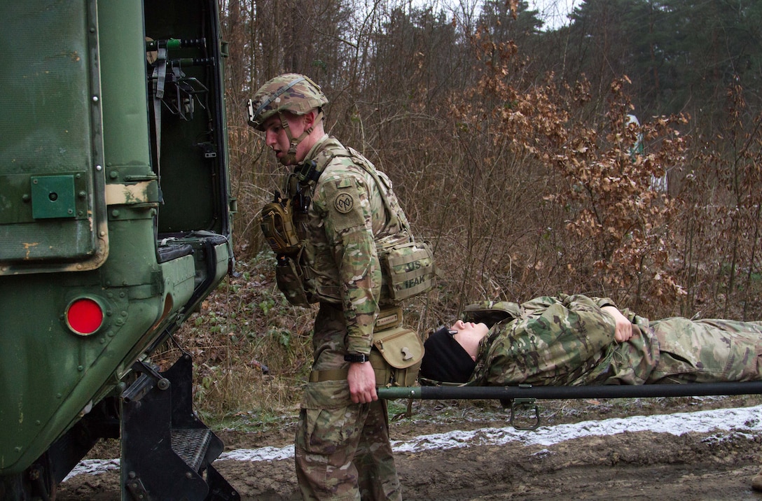 A soldier holding a person on a stretcher approaches a vehicle.