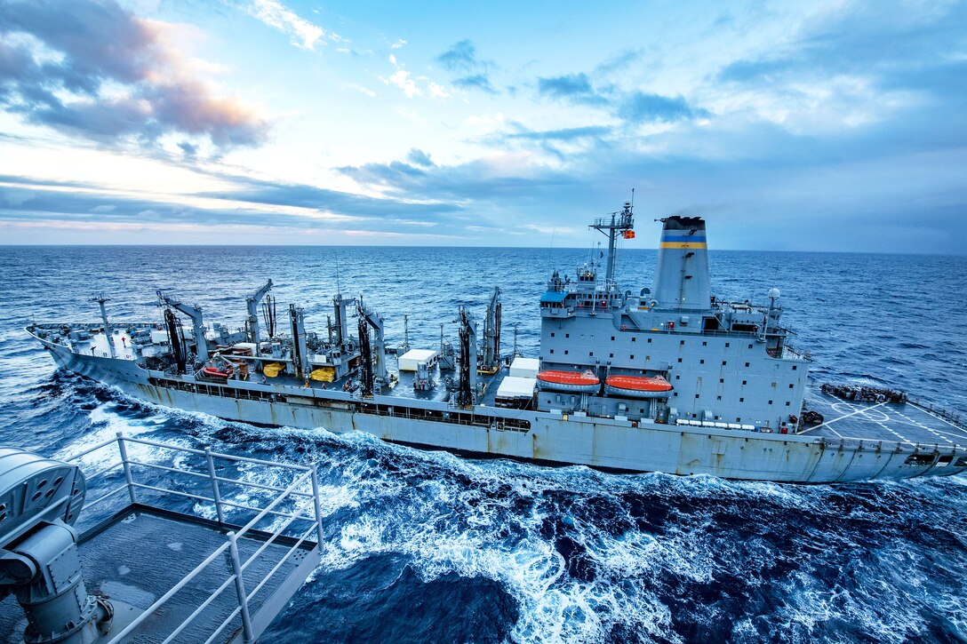 A fleet replenishment oiler travels beside another ship in the sea.