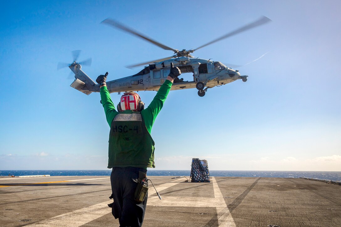 Navy Petty Officer 3rd Class Chase Weber directs an MH-60S Sea Hawk helicopter.