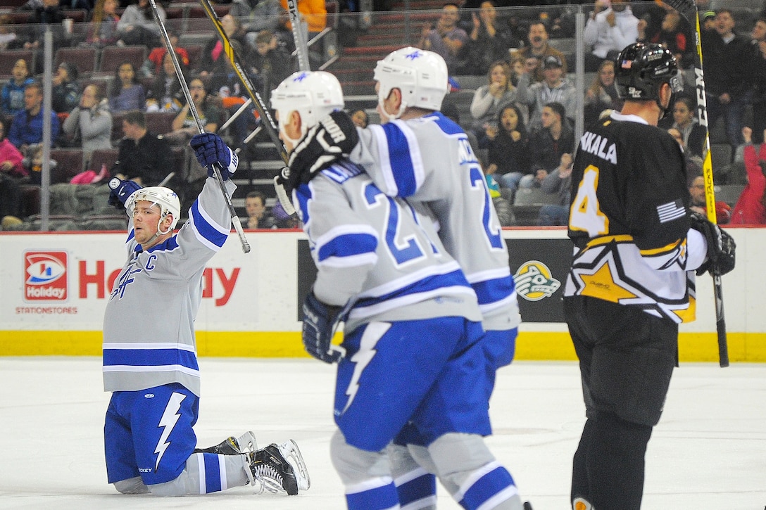 Airmen raise their hockey sticks and celebrate after scoring a goal.