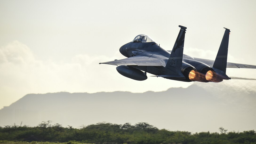 A fighter jet takes off with mountains in the background.