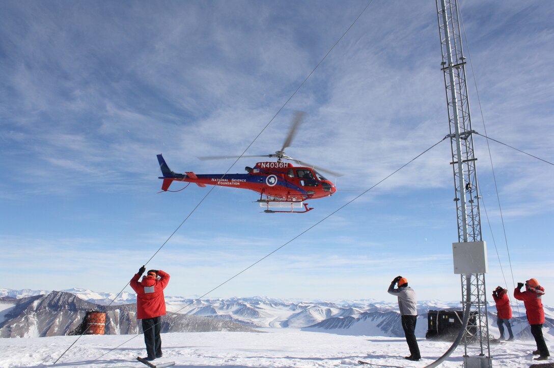 Battling high winds and frigid temperatures, seismic maintainers from the Air Force Technical Applications Center, Patrick AFB, Fla., receive fuel resupply via helicopter from the National Science Foundation at AFTAC’s repeater site at Mt. Newell, Antarctica.  The Airmen use the fuel to power the batteries that are the energy source for their seismic data collection equipment, radios and other communications functions.  Pictured from left to right:  Senior Airman Richard Westra, Raymond Richards, Staff Sgt. Jeremy Hannah and Senior Airman Andrew Pouncy.  (U.S. Air Force photo by Brian Fox)