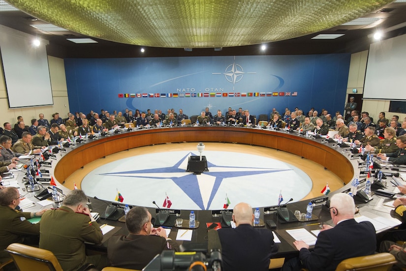 Dozens of men sit around a large circular table in a meeting room.