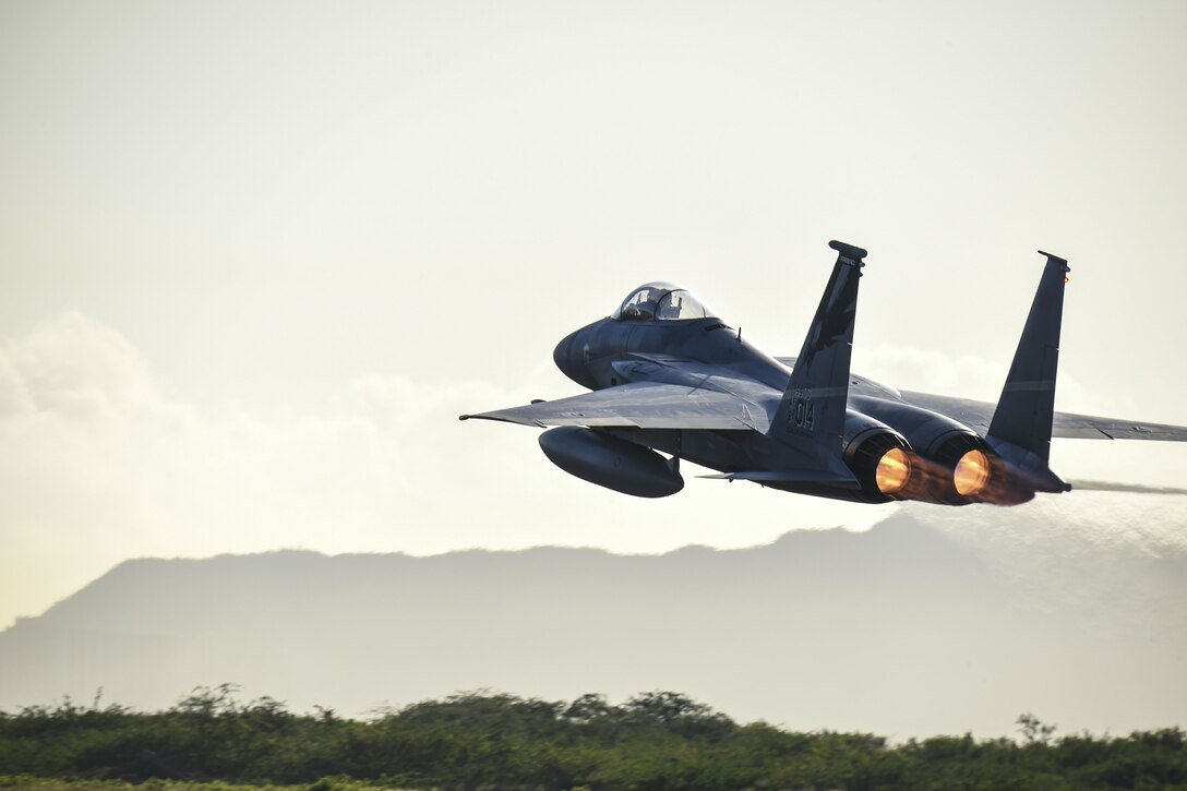 A fighter jet takes off with mountains in the background.