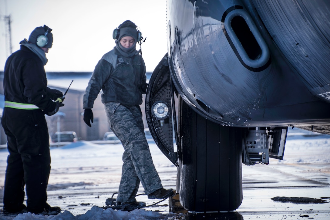 Airman First Class Sophia Marshall, left, adjusts a wheel chock under the tire of a C-130H Hercules aircraft.