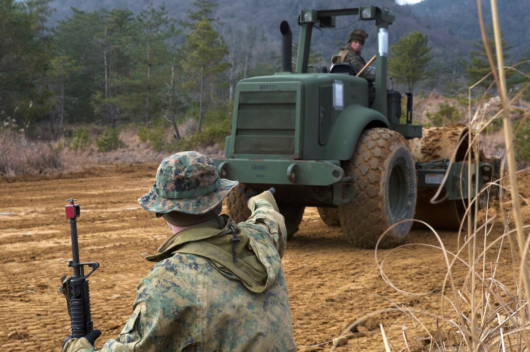 A Marine provides security and directs a heavy equipment operator leveling out terrain during exercise Kamoshika Wrath 18-1.