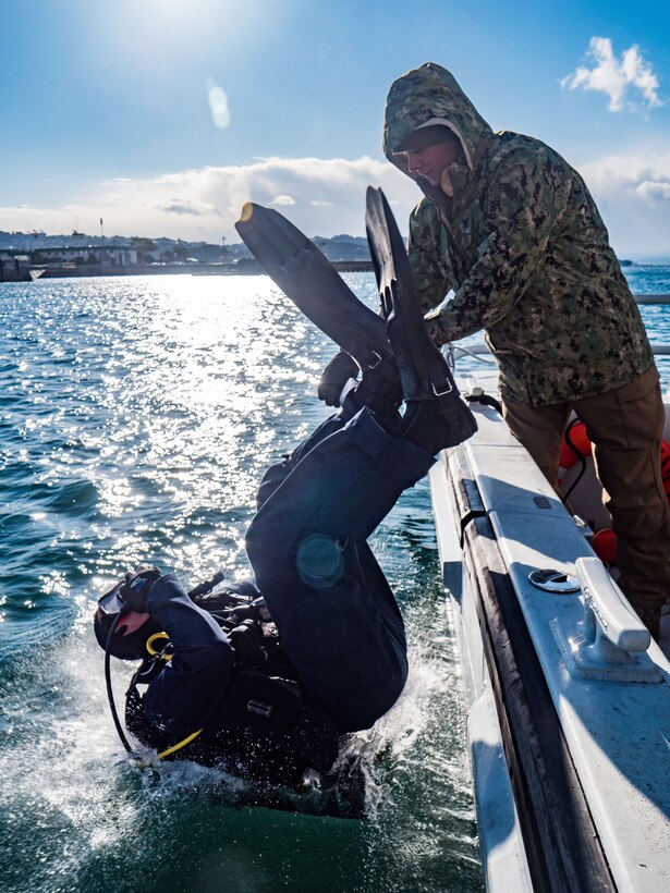 A seaman does a backward roll into the water.