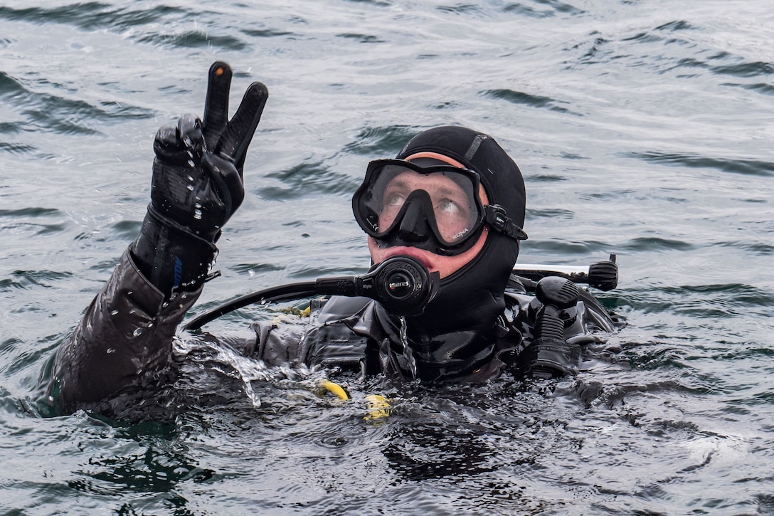 A Navy diver makes a signal before going underwater.