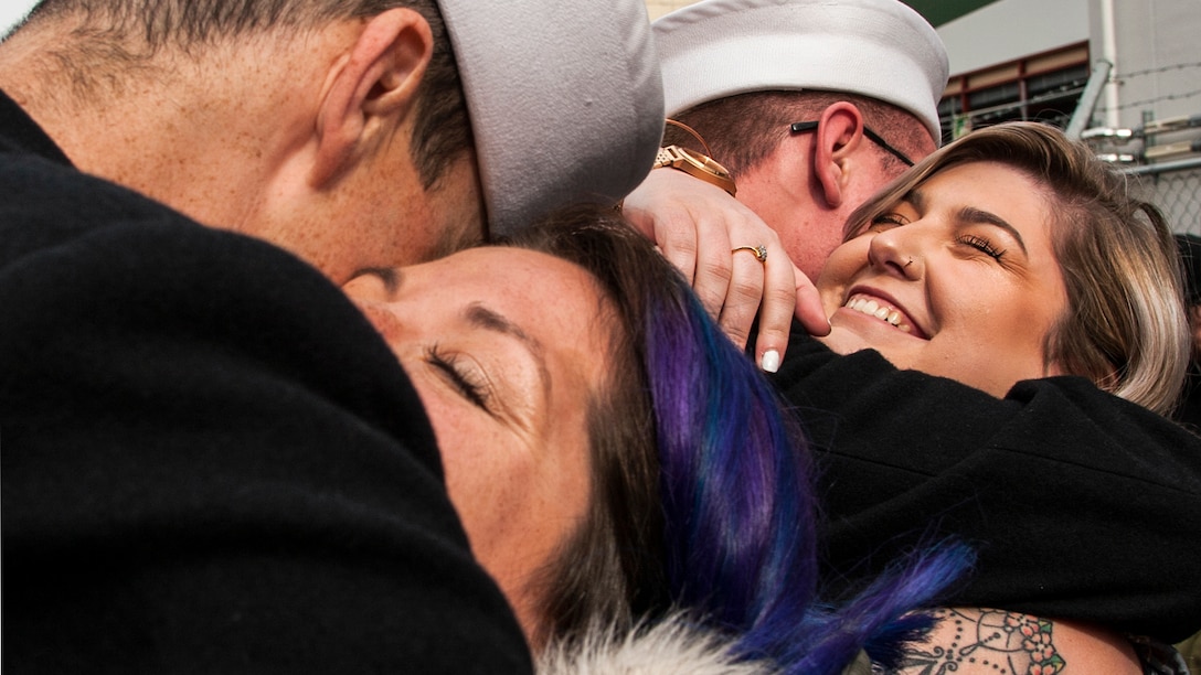 Two couples standing near each other hug.