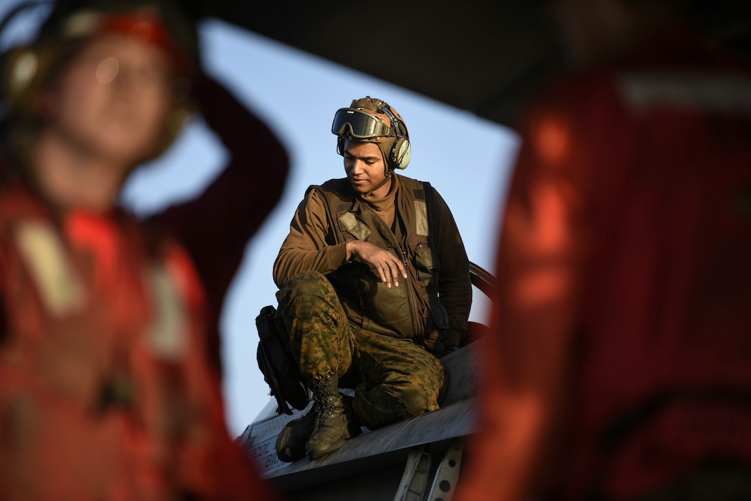 A Marine, framed by two service members in red, kneels on an aircraft.