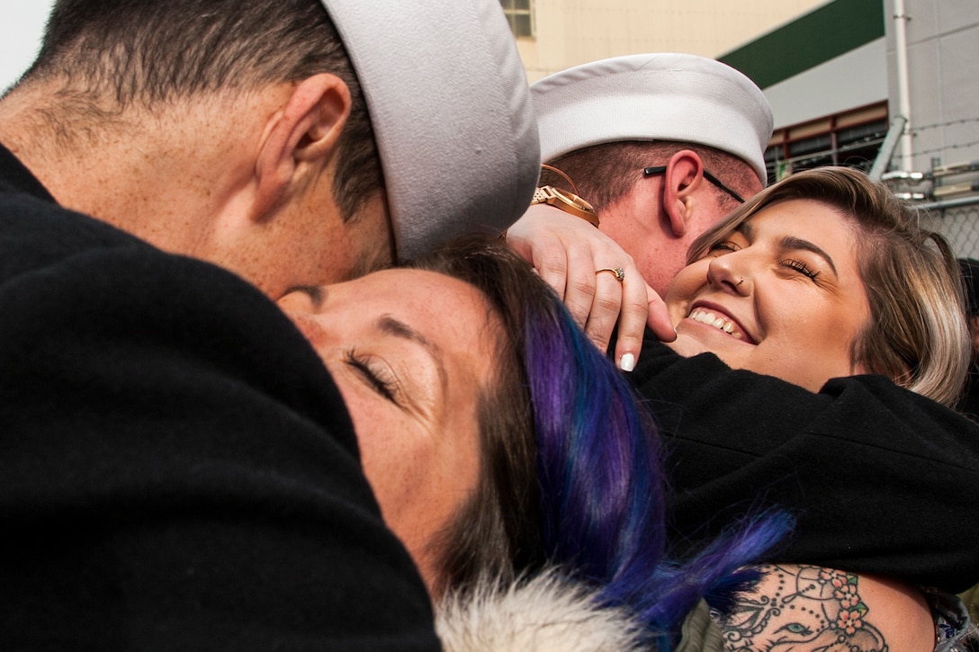 Two couples standing near each other hug.