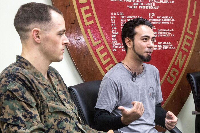 A Marine and a civilian sit together on a stage.