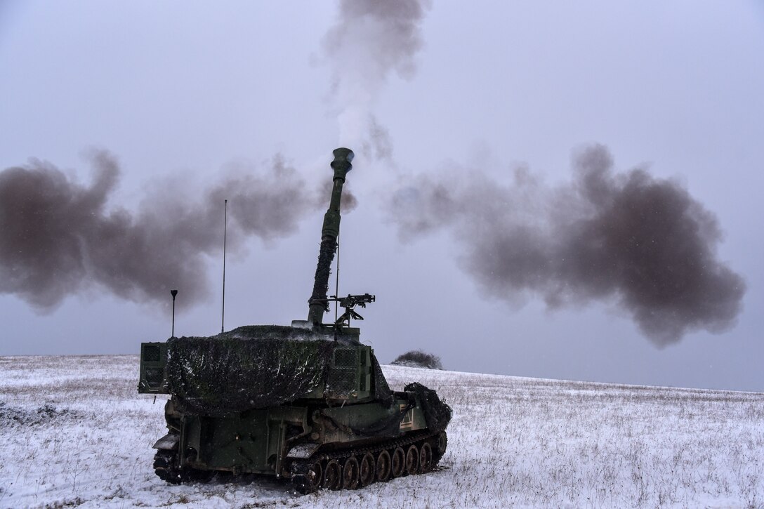 An M109A6 Paladin howitzer is fired during a live fire exercise in a snow-covered field.