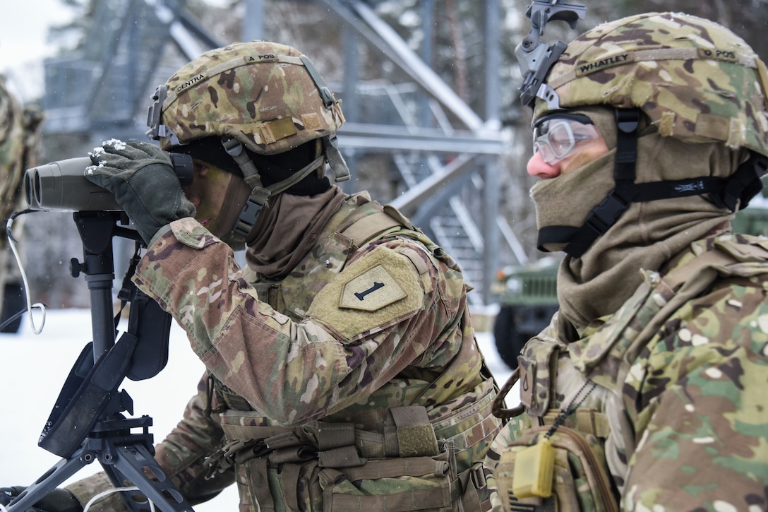 Two soldiers observe the impact zone from afar during a live fire exercise.