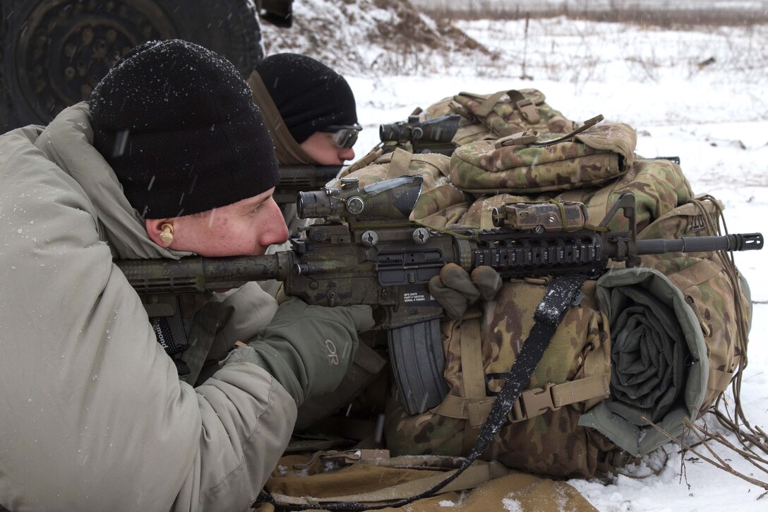 Two soldiers fire M4 rifiles on a snow-covered range.