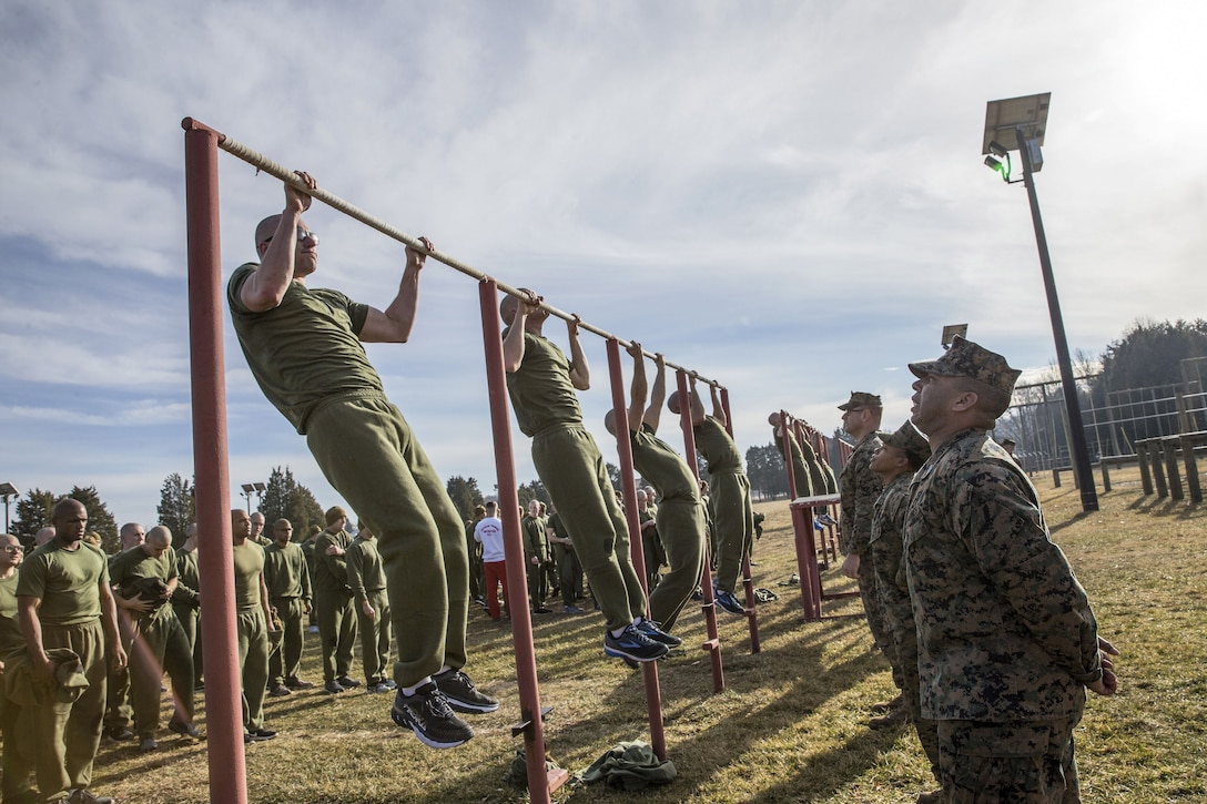 A row of Marines do pullups as fellow Marines observe.