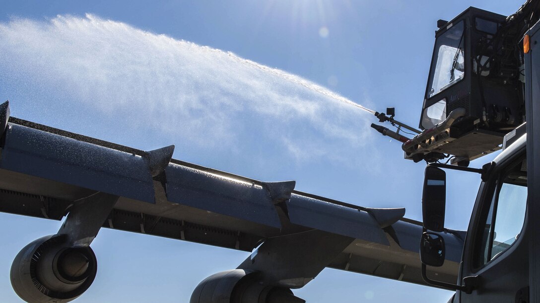 Liquid blasts out from a hose over an aircraft wing.