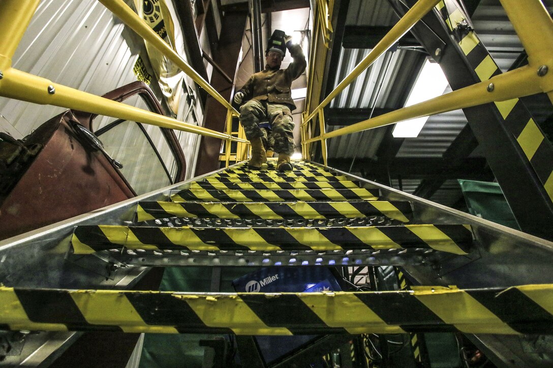 A soldier, shown from the bottom of stairway, walks down its yellow and black striped metal steps.