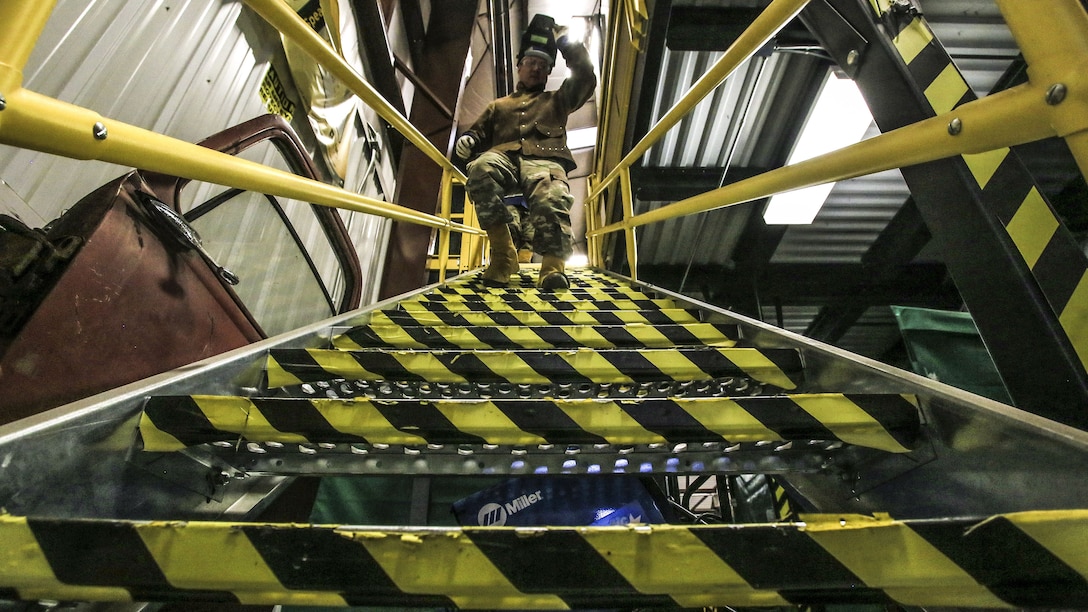 A soldier, shown from the bottom of stairway, walks down its yellow and black striped metal steps.