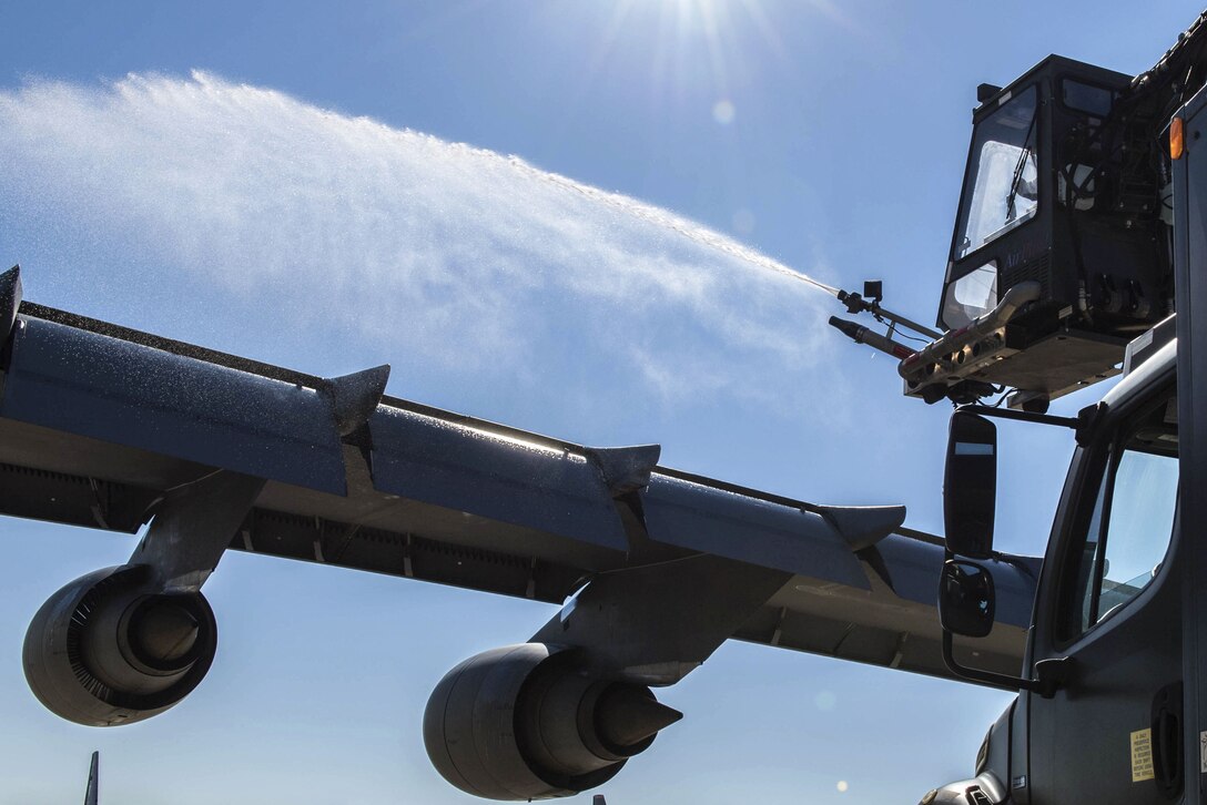 Liquid blasts out from a hose over an aircraft wing.