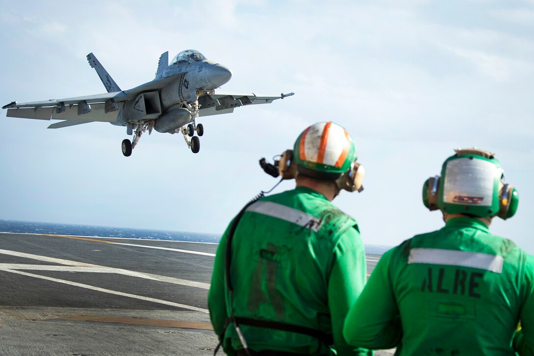 Sailors observe as an F/A-18F Super Hornet aircraft prepares to land on the flight deck of the USS Gerald R. Ford.