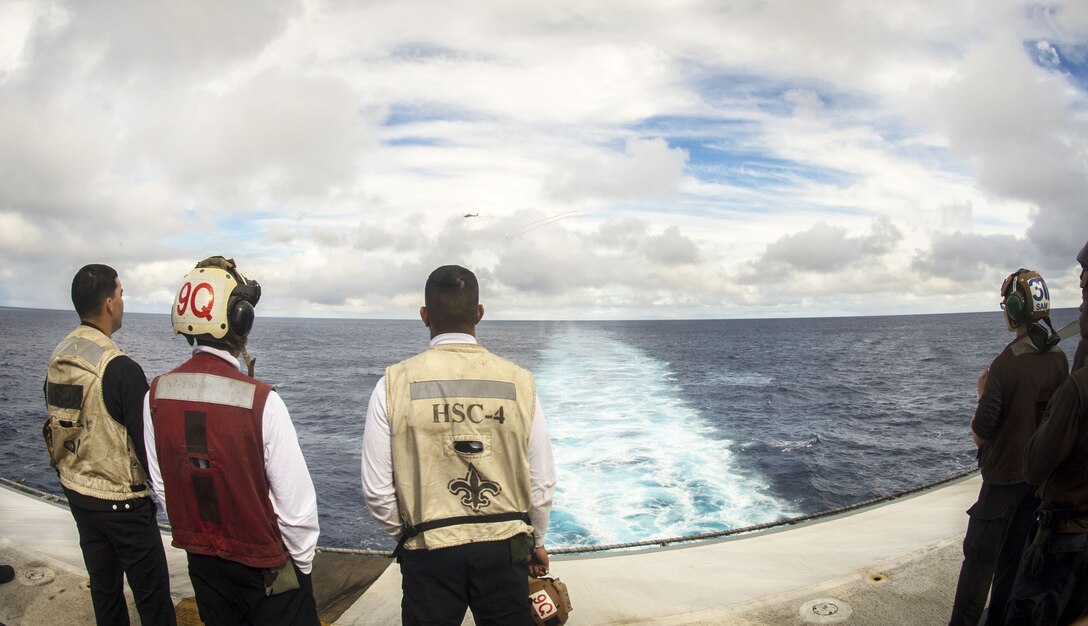 Sailors observe a live-fire evolution being conducted from an MH-60S Sea Hawk helicopter.