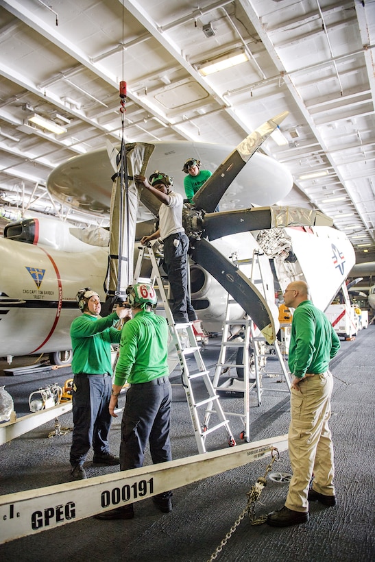 Sailors perform maintenance on an E-2C Hawkeye in the hangar bay aboard the Nimitz-class aircraft carrier USS Carl Vinson.