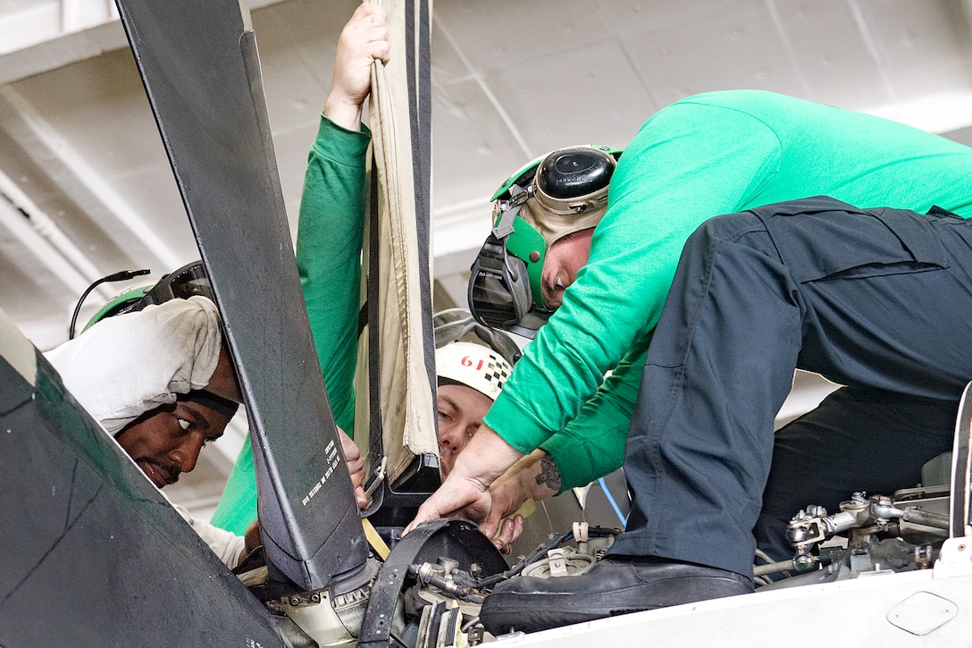 Sailors perform maintenance on an E-2C Hawkeye in a hangar bay.