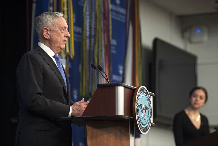 Defense Secretary James N. Mattis stands behind a podium speaking with another person in the background.
