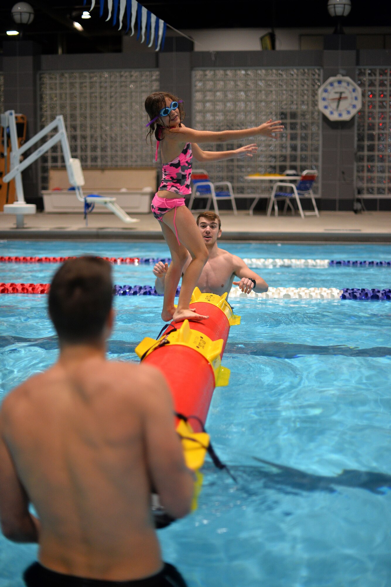 Trinity Hopwood attempts to maintain balance on a synthetic log with the assistance of two lifeguards at the base pool located inside the Offutt Field House on Jan. 13, 2018.