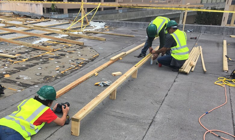 Contractors working for the U.S. Army Corps of Engineers in Puerto Rico install the first Blue Roof on the Multy Medical Facilities in San Juan. Having the roof protected will allow the hospital to open additional patient beds/rooms that were previously unavailable because of the damaged roof. Brigida Sanchez, a Corps public affairs specialist from the Corps' Walla Walla District headquarters, in Walla Walla, Washington, (left) photographically documents the event.