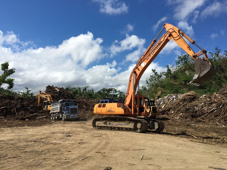 An excavator repositions for operations unloading and loading trucks Nov. 24, 2017, at the Trujillo Alta temporary disposal site in Puerto Rico. Temporary sites serve as municipal collection points for woody debris before it’s reduced to mulch or transferred to another location for permanent deposition (mulch recycling site or landfill).