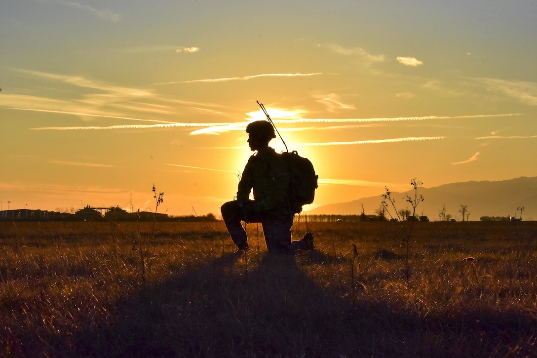 A soldier kneels in front of a sunset