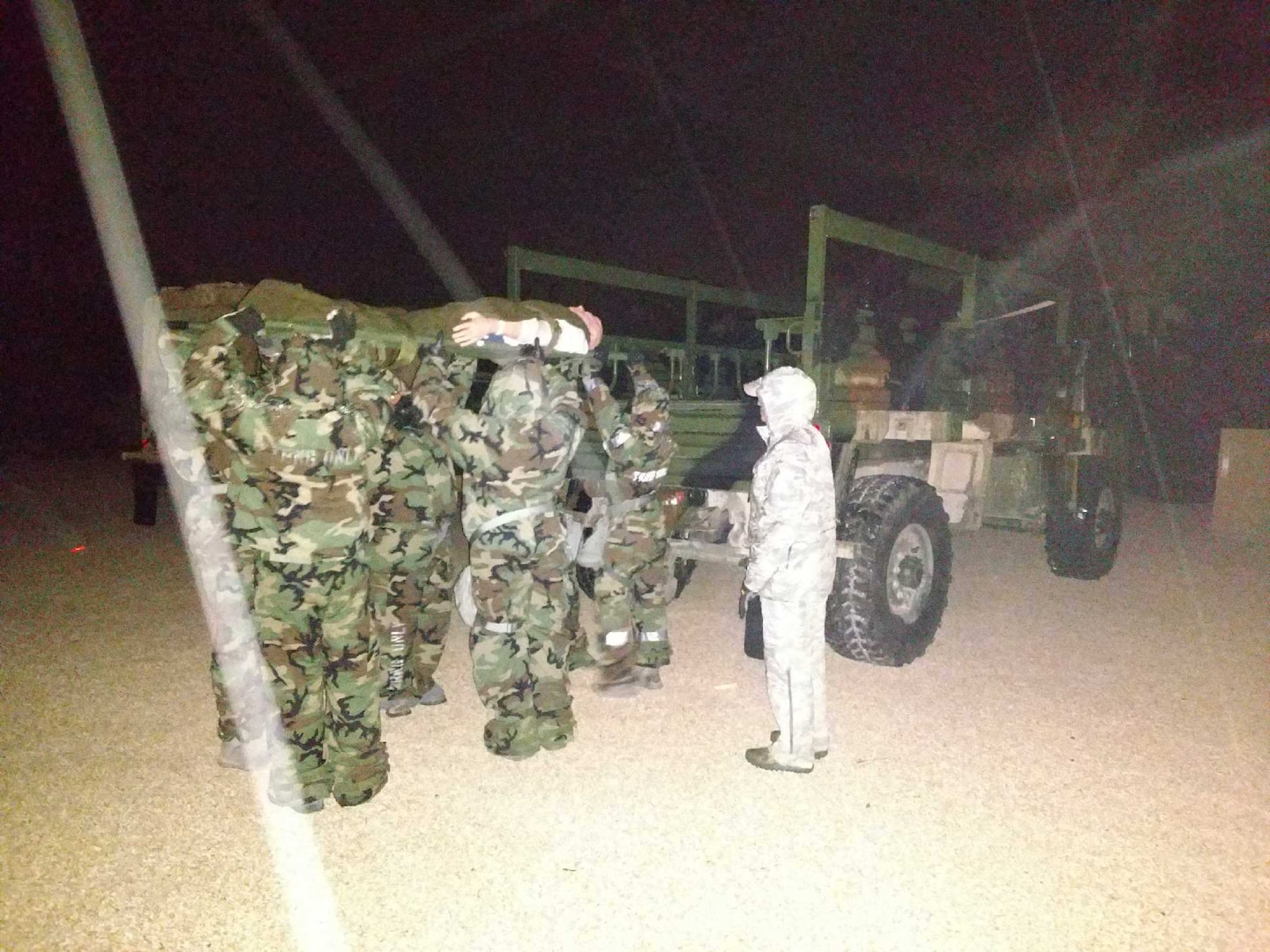 Airmen medics wearing mission oriented protective posture gear load a mannequin on to a transport vehicle during nighttime training at Joint Base San Antonio-Camp Bullis. The training is comprised of scenarios focused on helping Airmen medics understand challenges that might occur during a chemical or biological event.
