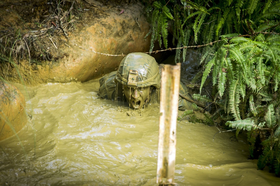 A mud-covered Marine gasps for breath while shoulder-deep in a mud pit.