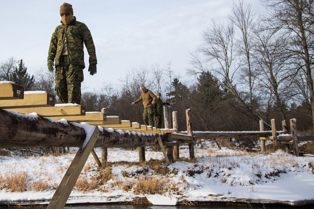 Marines walk across a wooden plank bridge.