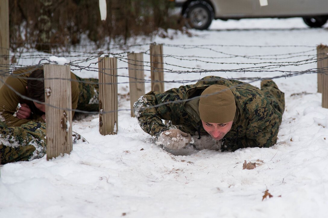 A Marine moves on his stomach below barbed wire.