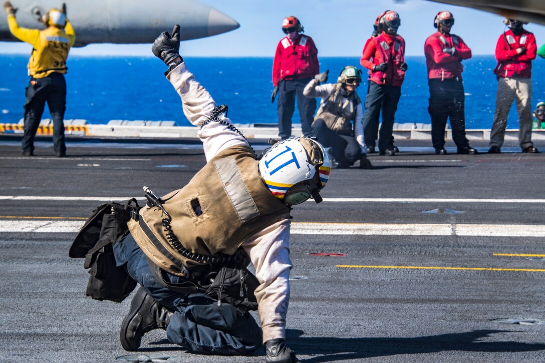 A sailor gives the signal to launch an aircraft.