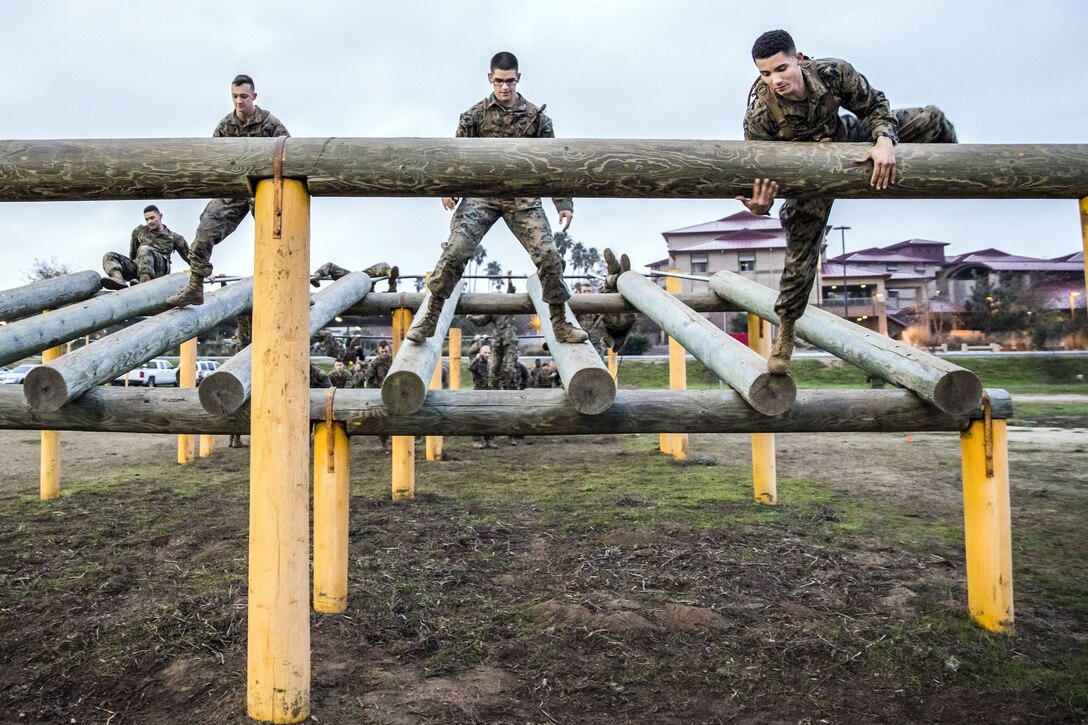 Three Marines stand on a log obstacle raised off the ground.
