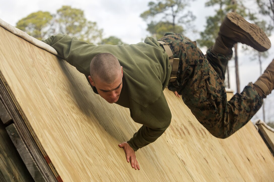 A Marine jumps over a wooden wall.